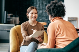 A young person holds a pen and paper while talking with an older person, smiling.