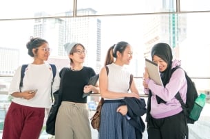 A group of four young Asian or Asian American women of diverse ethnicities standing in an academic building.