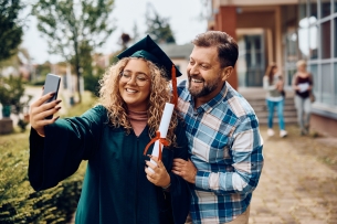 Happy university graduate and her father smile while taking selfie.