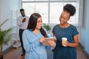 Two businesswomen talk in the office with digital tablet