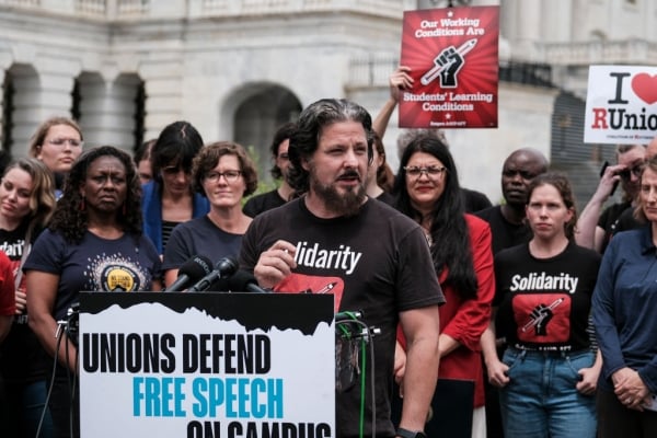 Faculty members and lawmakers stand outside the Capitol Building behind a podium that says Unions Defend Free Speech on Campus