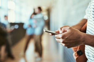 A close-up image of the hands of a student as they text on their phone.