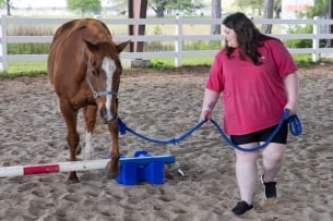 A student leads a horse over a low jump in an arena