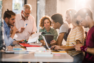 A college professor teaches a group of five students gathered around a table.